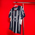 Navy and white striped soccer jersey on a hanger against a bright red wall, showing sponsor logos.