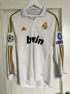 White Real Madrid soccer jersey on a hanger with gold trim, adidas logo, and bwin sponsor.