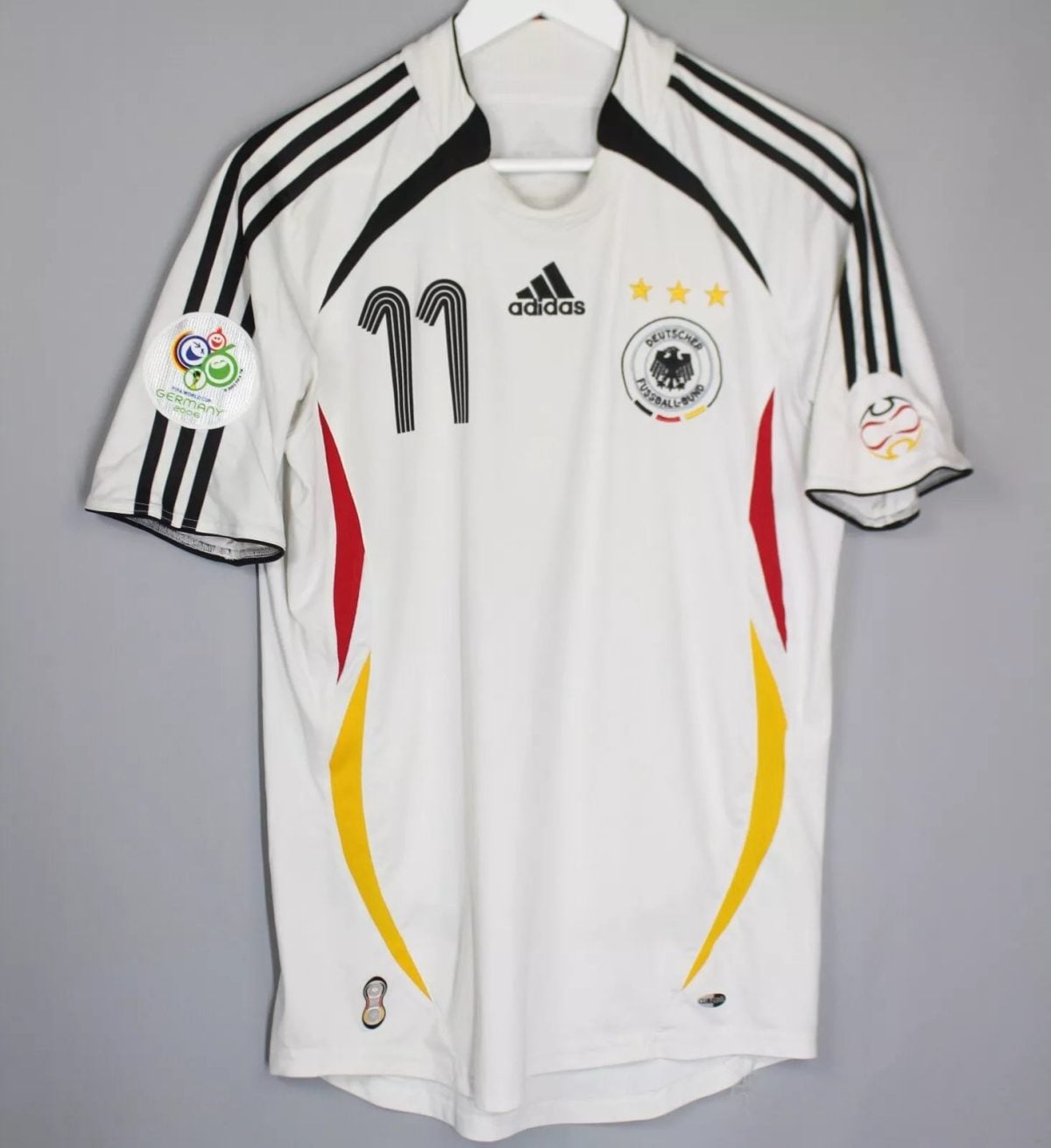 White Germany national football jersey on a hanger, with black Adidas stripes, number 11, crest and three gold stars on the chest.