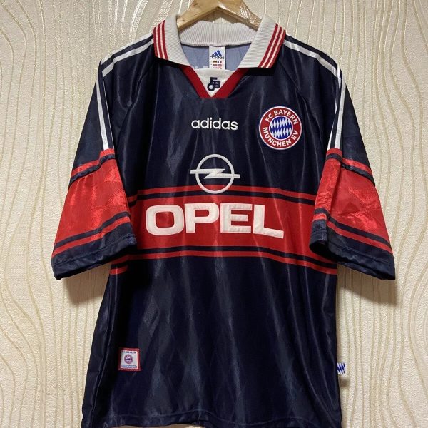 Navy Bayern Munich soccer jersey on hanger with red Opel sponsor and white Adidas logos, FC Bayern badge on chest.