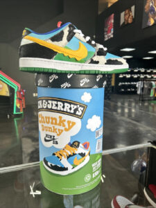 s-l1600_6ff9f74c-063c-41c2-9ce2-7e621d0df5be | UAE SPORT STORE Nike SB Dunk Low sneaker with cow-print panels, yellow swoosh, and blue/green accents perched on a Ben & Jerry's Chunky Dunky display in a sneaker store