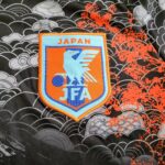 s-l1600_7_d74b71f1-b716-41d0-a4fb-db4453be9b6d | UAE SPORT STORE Patch showing Japan Football Association (JFA) emblem on light blue and orange, with 'JAPAN' at top, sewn onto patterned fabric background.