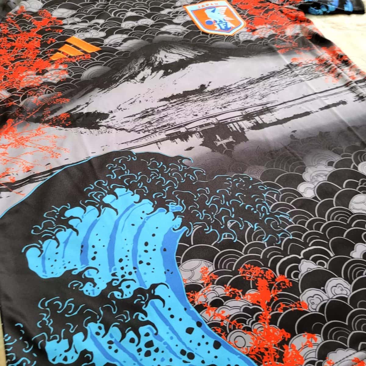 Decorative textile with bold blue waves, a black-gray seigaiha pattern, and bright orange floral accents.