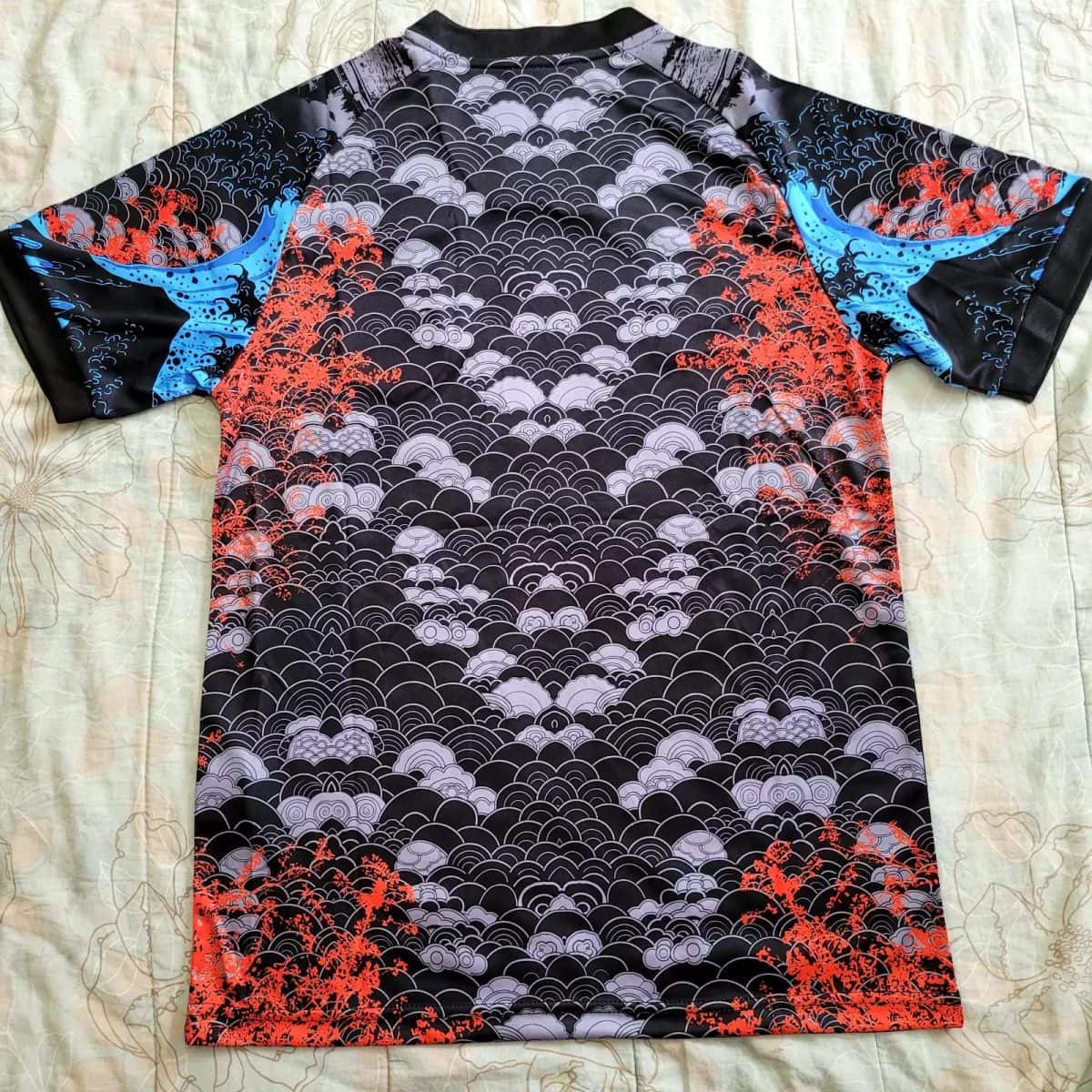 Back view of a short-sleeve athletic jersey with black/gray wave pattern and red coral accents; blue panels on the sleeves.