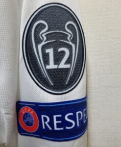 s-l500_15_08b562d8-6659-4480-9f5a-0b41170c2bd1 | UAE SPORT STORE Close-up of a white football jersey sleeve with a black shield badge displaying the number 12 and a blue band reading UEFA RESPECT.