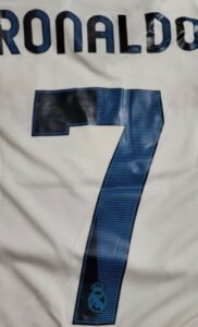 Back view of a white Real Madrid jersey with the name Ronaldo and a large blue number 7, Real Madrid crest near the base of the number.