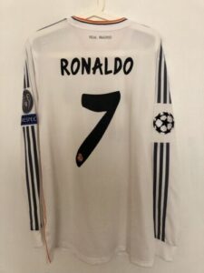 White Real Madrid home jersey with the name RONALDO and number 7 on the back, hanging on a hanger, with Champions League patch on the left sleeve.