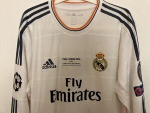 White Real Madrid football jersey for the 2014 Lisbon final featuring Adidas logo, Fly Emirates sponsor, Real Madrid crest, and UEFA Champions League patches.