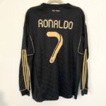 Black Real Madrid Ronaldo jersey with gold 'RONALDO' name and number 7 on the back, hanging against a wall.