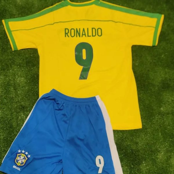 Yellow Brazil soccer jersey with 'RONALDO' and number 9 laid over blue shorts on grass, celebrating a football kit set up.