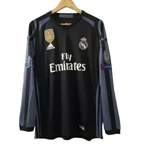 Black Real Madrid jersey on a hanger with Fly Emirates sponsor and team crest visible, long sleeves with blue-gray stripes.