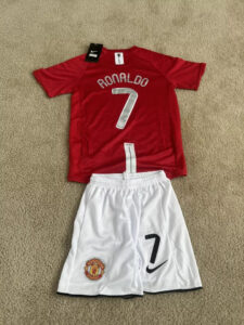 s-l960_4 | UAE SPORT STORE Red Manchester United jersey with number 7 and 'RONALDO' on the back, laid over white shorts with the club crest.