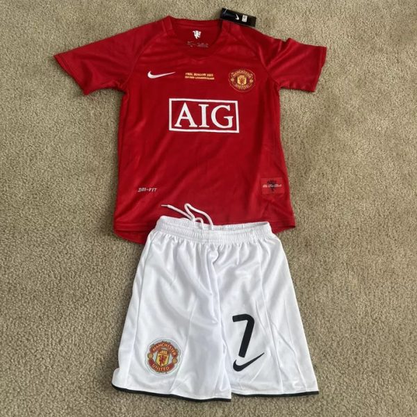 Manchester United red home jersey with AIG sponsor and crest, laid on a carpet beside white shorts with a large '7' and Nike swoosh.