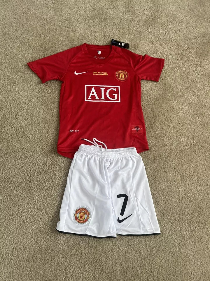 s-l960_5 | UAE SPORT STORE Manchester United red home jersey with AIG sponsor and crest, laid on a carpet beside white shorts with a large '7' and Nike swoosh.