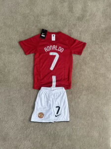 s-l960_6 | UAE SPORT STORE Red Ronaldo #7 football jersey laid on beige carpet with white Manchester United shorts showing the number 7 and club crest nearby.