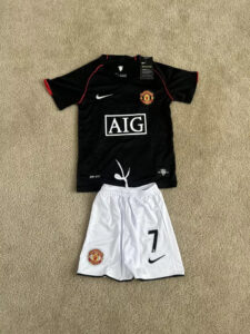 s-l960_8850c579-7597-4c4c-9b44-6bbf1927885b | UAE SPORT STORE Manchester United kit laid out: black jersey with red piping, white Nike swoosh, AIG sponsor, and white shorts with the number 7 and club crest.