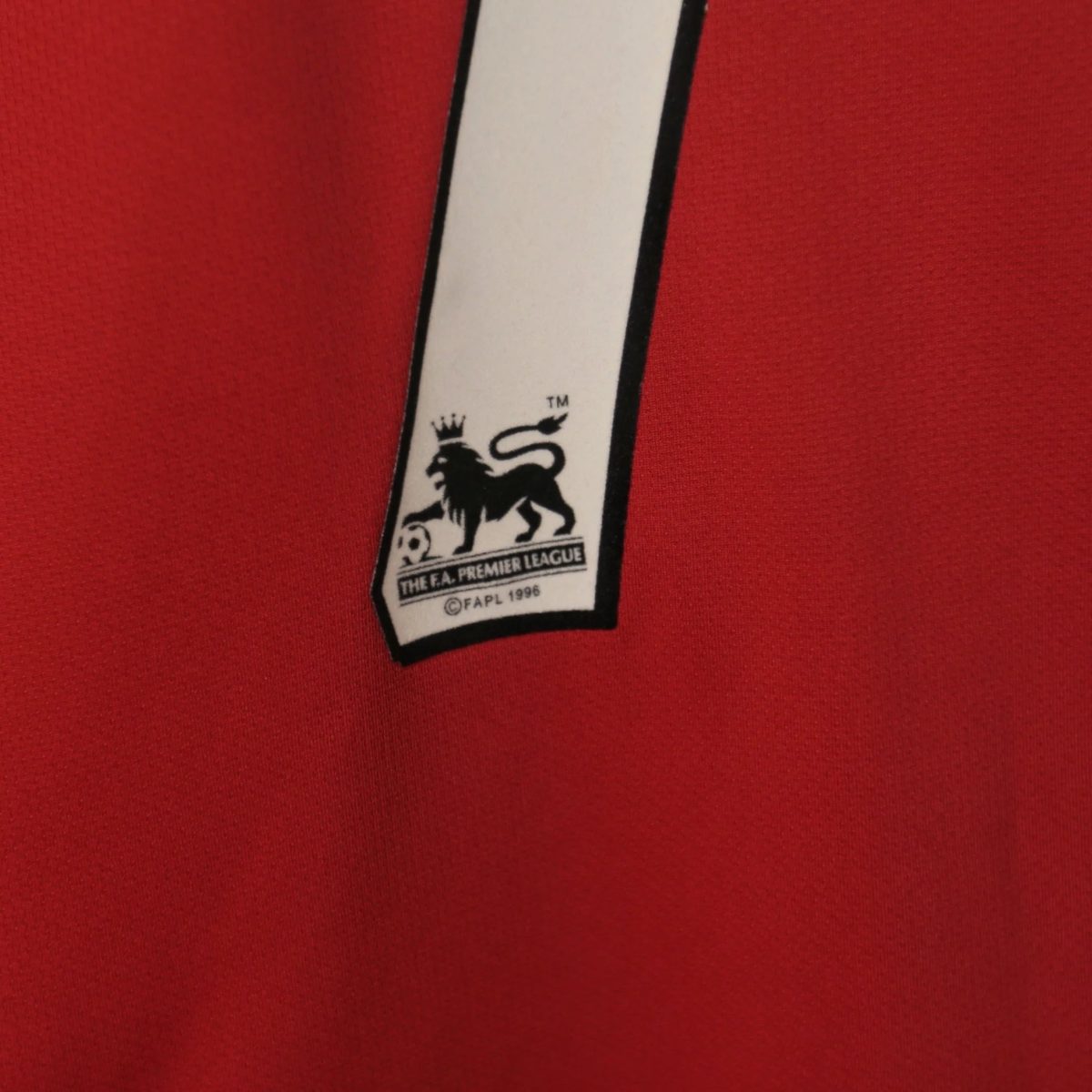 Close-up of a white tag with a crown and lion logo on red fabric in the background.