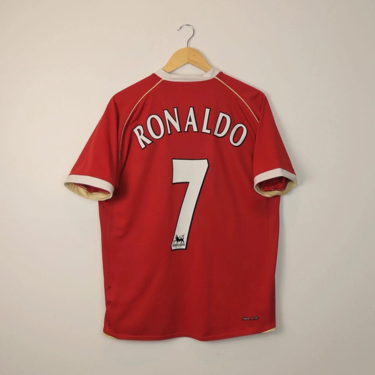 Red sports jersey hanging on a wooden hanger, back shows 'RONALDO' and the number 7 on a pale wall.