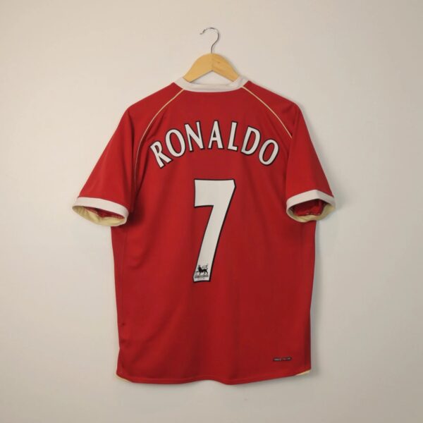 Red sports jersey hanging on a wooden hanger, back shows 'RONALDO' and the number 7 on a pale wall.
