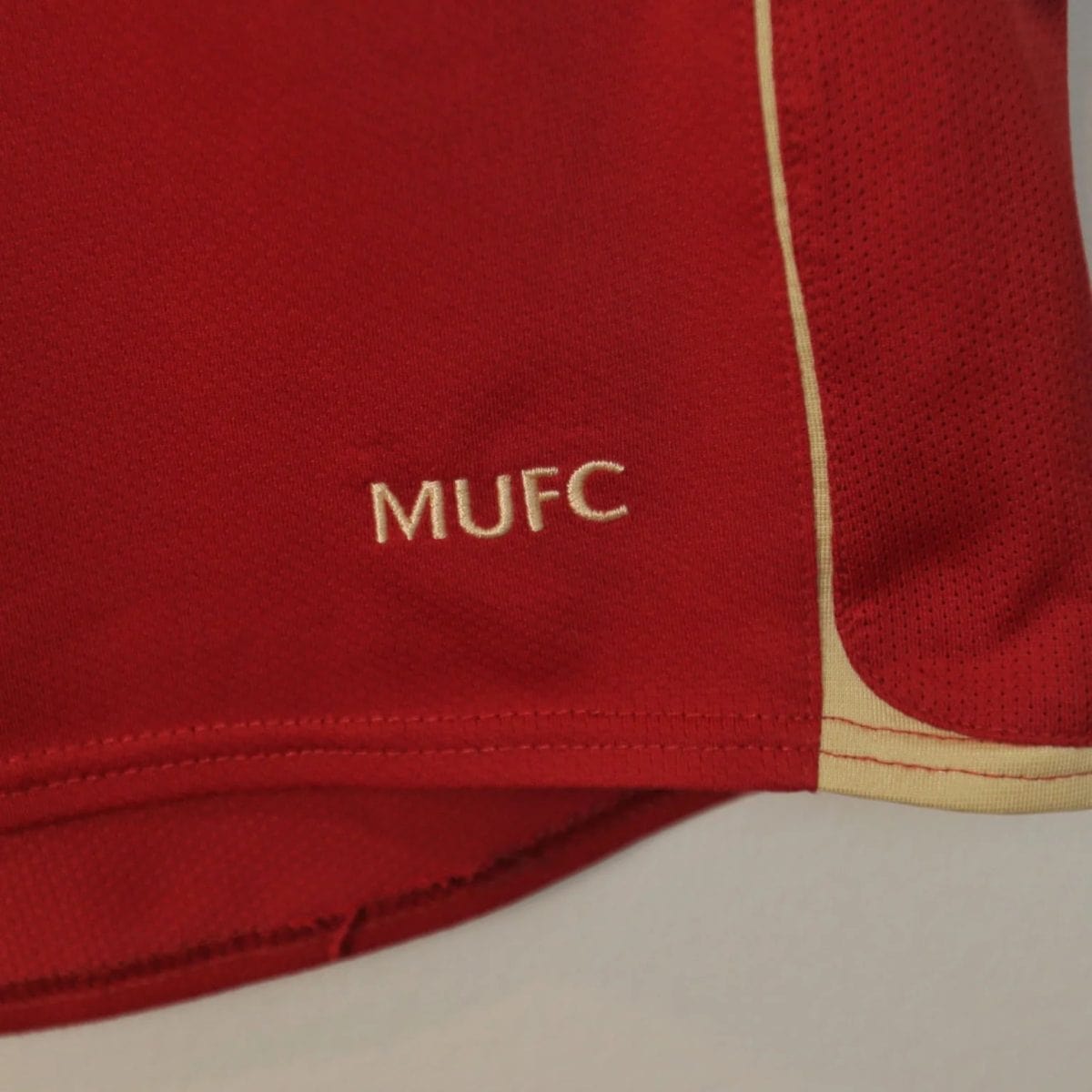 Close-up of red fabric with white embroidered letters 'MUFC' on a sports jersey.