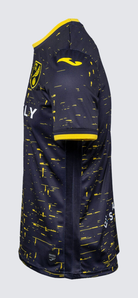 Side view of a navy blue soccer jersey with a yellow speckled pattern, yellow collar trim, and a club crest on the chest.