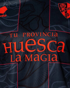 Close-up of a dark sports jersey with red text reading 'tu PROVINCIA Huesca La Magia' and a small team crest visible in the upper right corner.