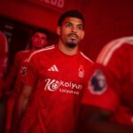 A male soccer player in a red jersey walking through a tunnel, looking ahead with a focused expression.