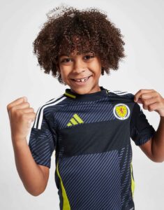 Smiling young boy in a Scotland football jersey poses with fists up, showing pride and excitement.