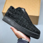 Black Louis Vuitton sneaker with monogram pattern, held in hand with a cardboard box in the background.