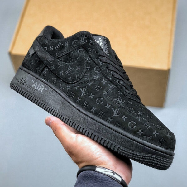 Black Louis Vuitton sneaker with monogram pattern, held in hand with a cardboard box in the background.
