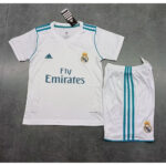 sg-11134201-7rccd-ltjuurg7v4xp92 | UAE SPORT STORE Real Madrid white home jersey with teal accents and shorts, featuring the Fly Emirates sponsor and club crest laid flat on a gray surface.