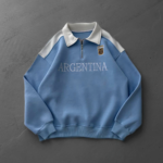 Light blue Argentina sweatshirt with a white collar and half-zip, featuring an AFA crest on the chest and 'ARGENTINA' across the front.
