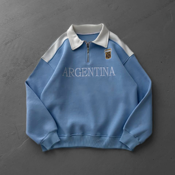 Light blue Argentina sweatshirt with a white collar and half-zip, featuring an AFA crest on the chest and 'ARGENTINA' across the front.
