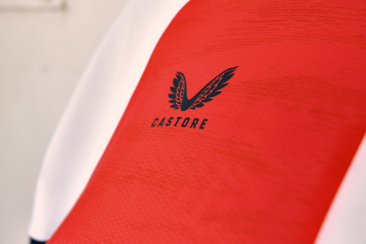 Close-up of red Castore sports jersey with a black wing logo and a white edge along the side.