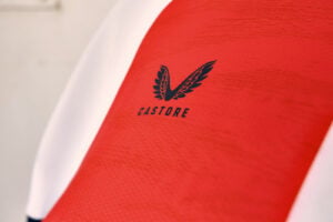 Close-up of red Castore sports jersey with a black wing logo and a white edge along the side.