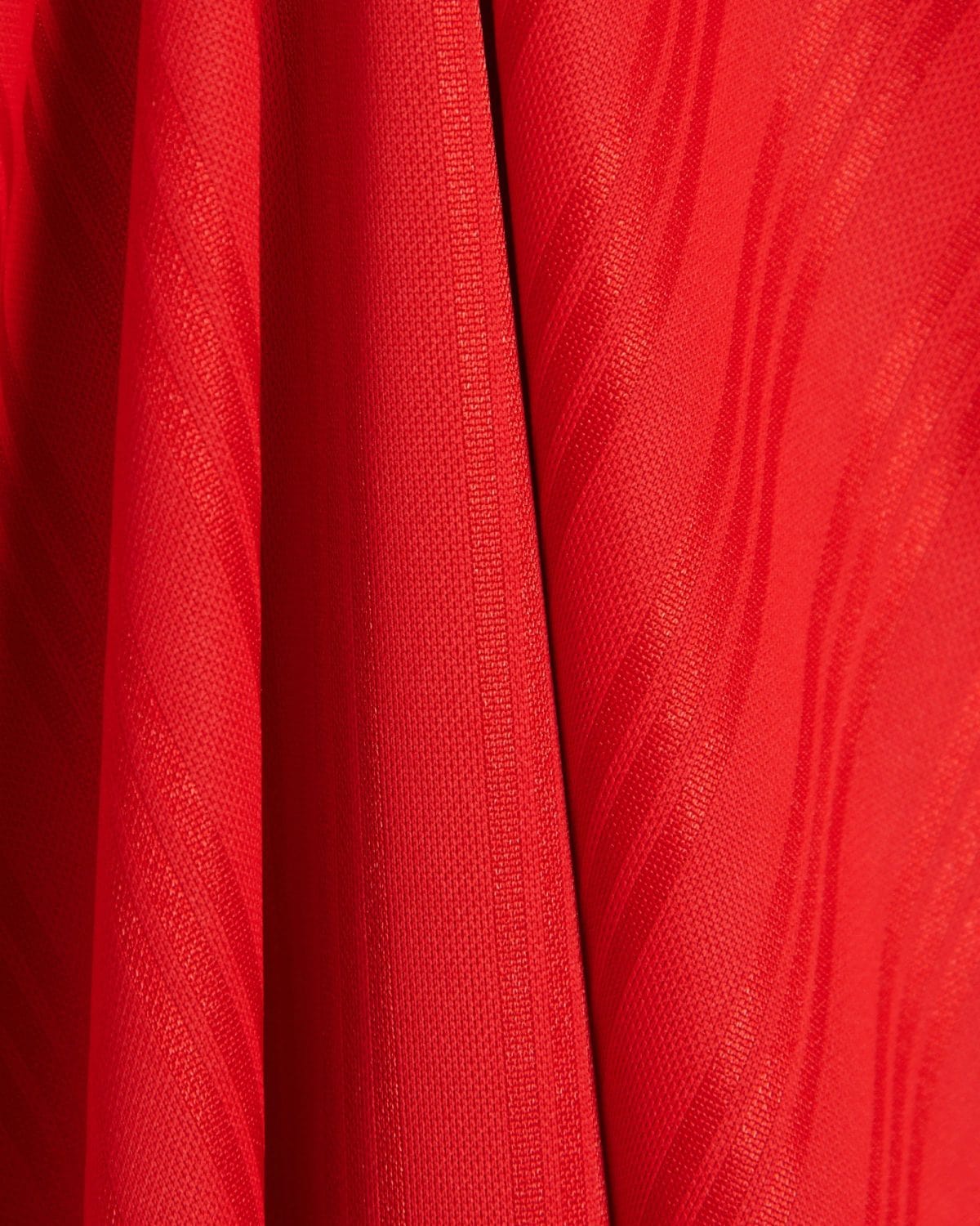 Close-up of bright red fabric with a textured knit and vertical folds or pleats