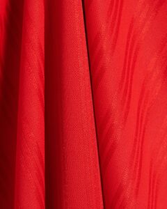 Close-up of bright red fabric with a textured knit and vertical folds or pleats