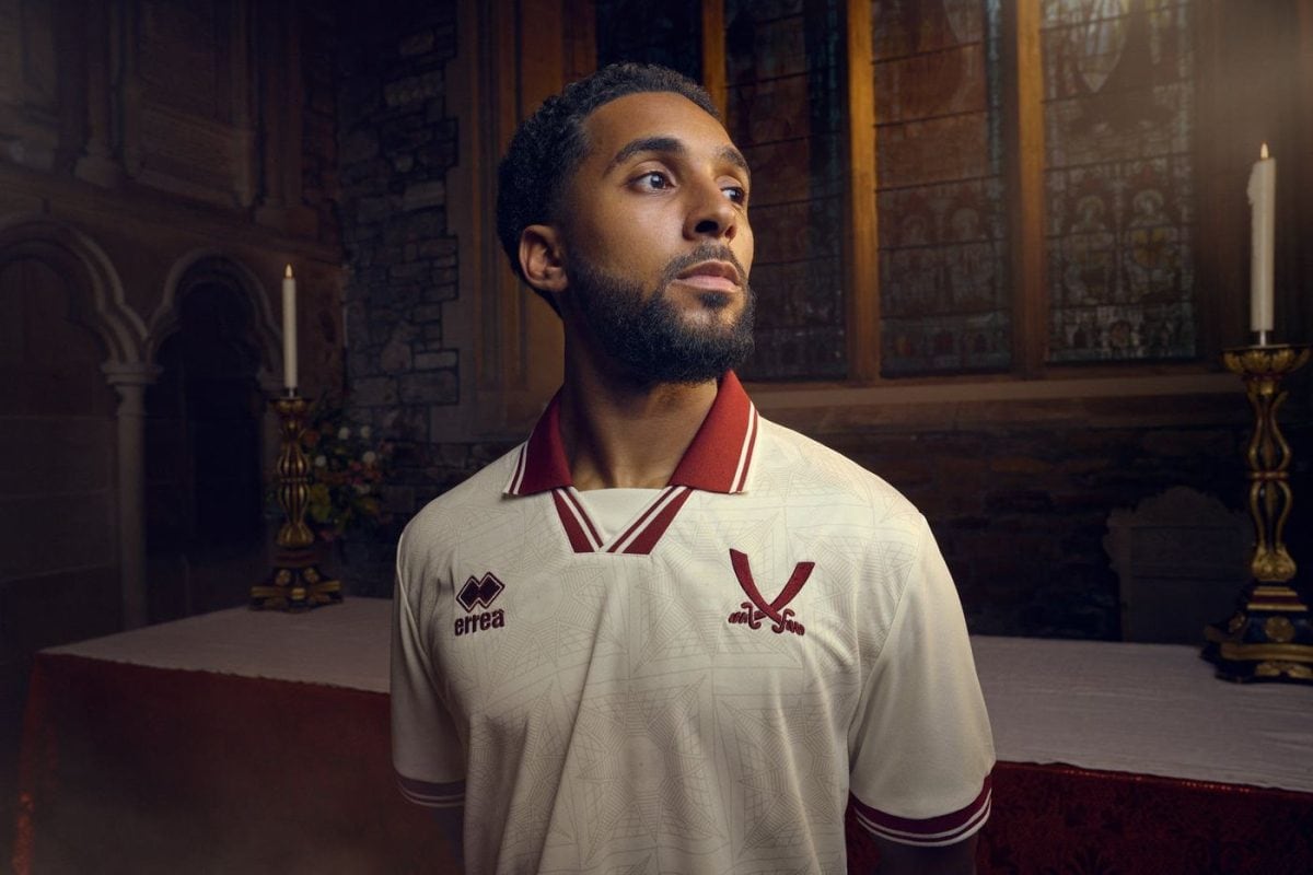 Portrait of a man in a white maroon-trim soccer jersey, standing by an altar in a church, looking to the side.
