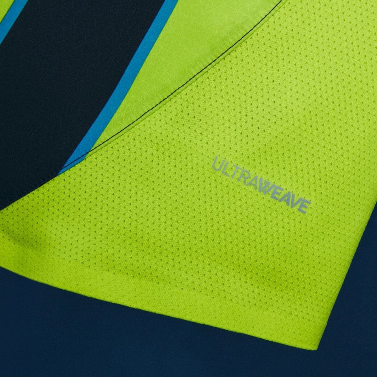 Close-up of neon yellow high-visibility fabric with a dark blue panel and blue stripe, showing the faint 'ULTRALIVE' text along the edge.
