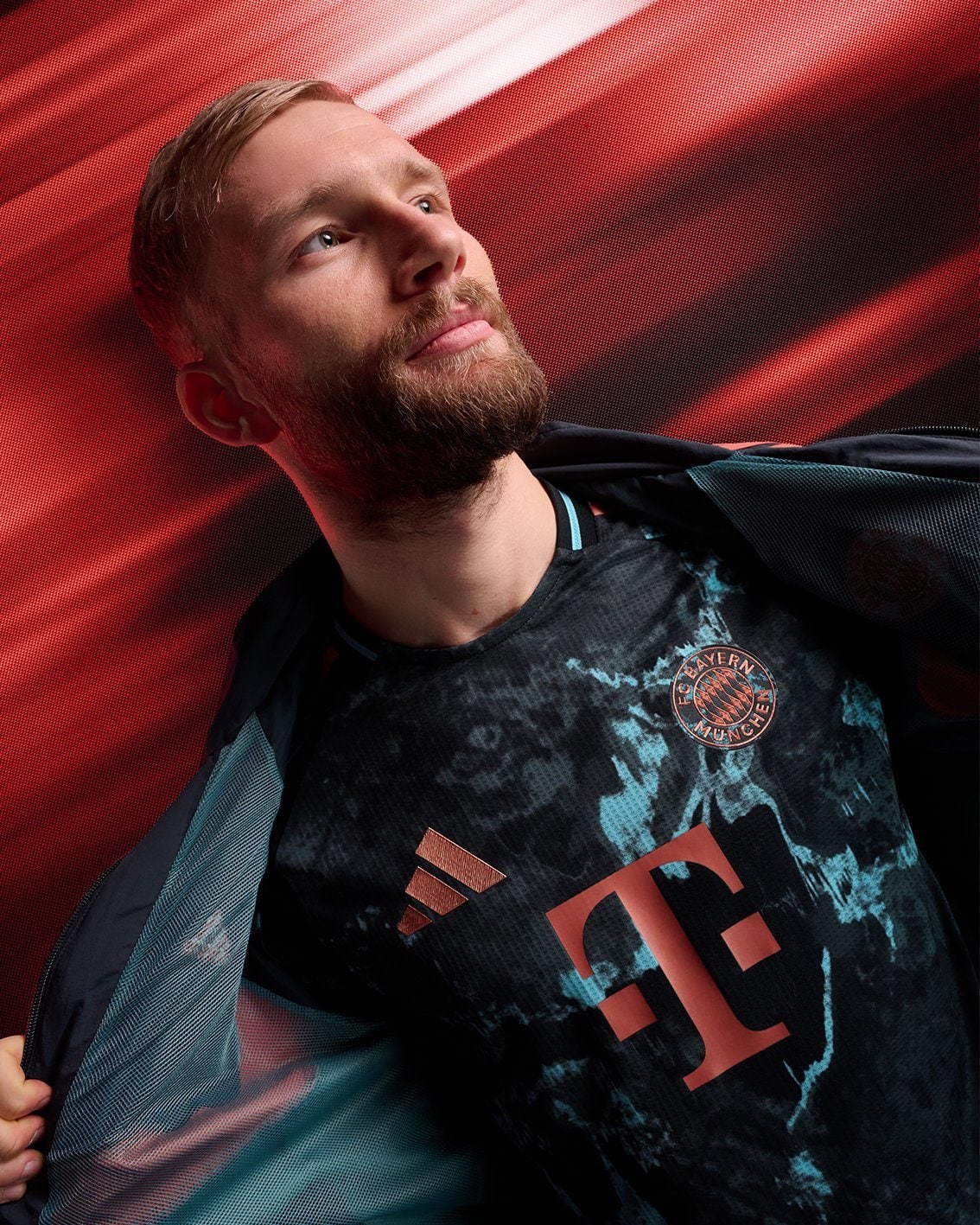 tUT04Xyv0z8sXTN | UAE SPORT STORE Portrait of a man with a beard wearing a Bayern Munich football jersey, looking upward against a red abstract background.