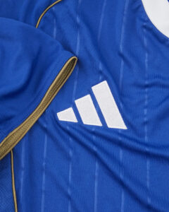 tewdnsdbo54fdz6jcl0o | UAE SPORT STORE Close-up of a blue sports jersey with white Adidas logo (three stripes) and a tan zipper visible on the left.