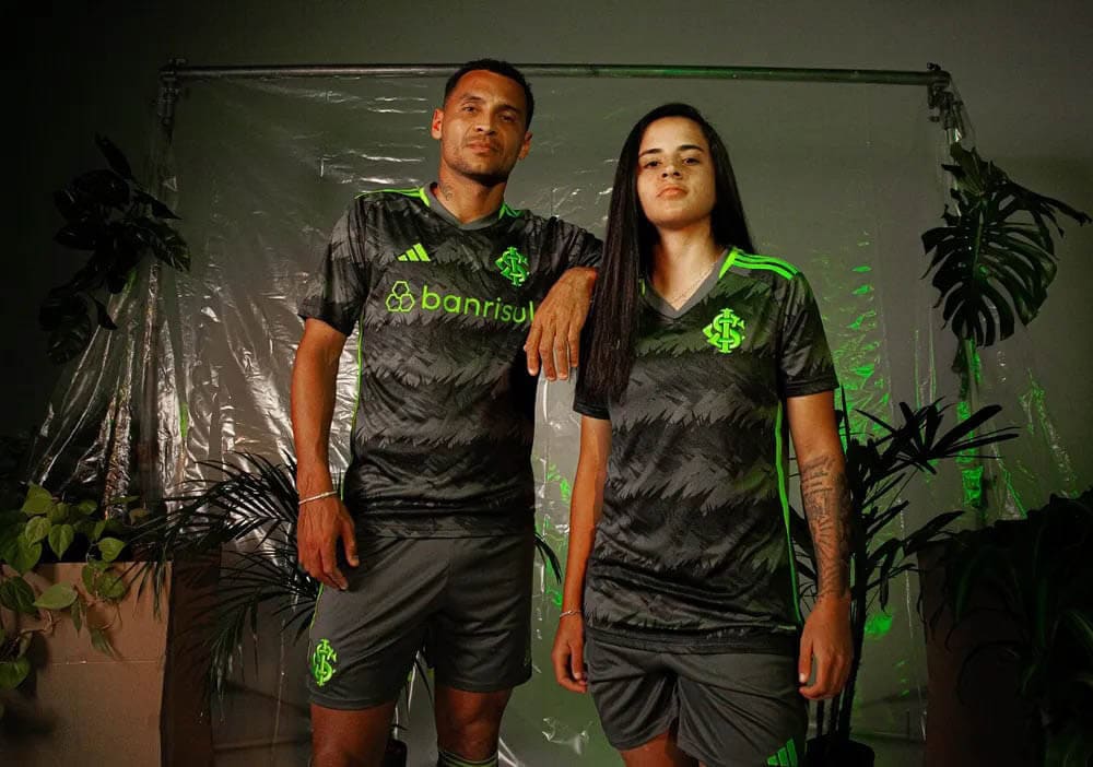 tnCgYLjFno4w3NO_6a005ba2-4065-4fe9-9619-a8aa89f403e2 | UAE SPORT STORE Two models in matching dark gray and neon green soccer jerseys pose together in a plant-filled studio backdrop.