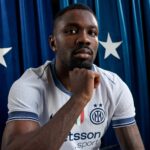 Close-up portrait of a Black man in an Inter Milan jersey, resting his chin on his hand against a blue backdrop with stars.
