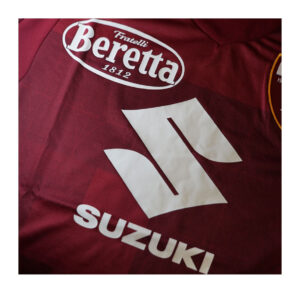 Close-up of a maroon sports jersey displaying white Beretta Fratelli 1812 and Suzuki logos on fabric edge.