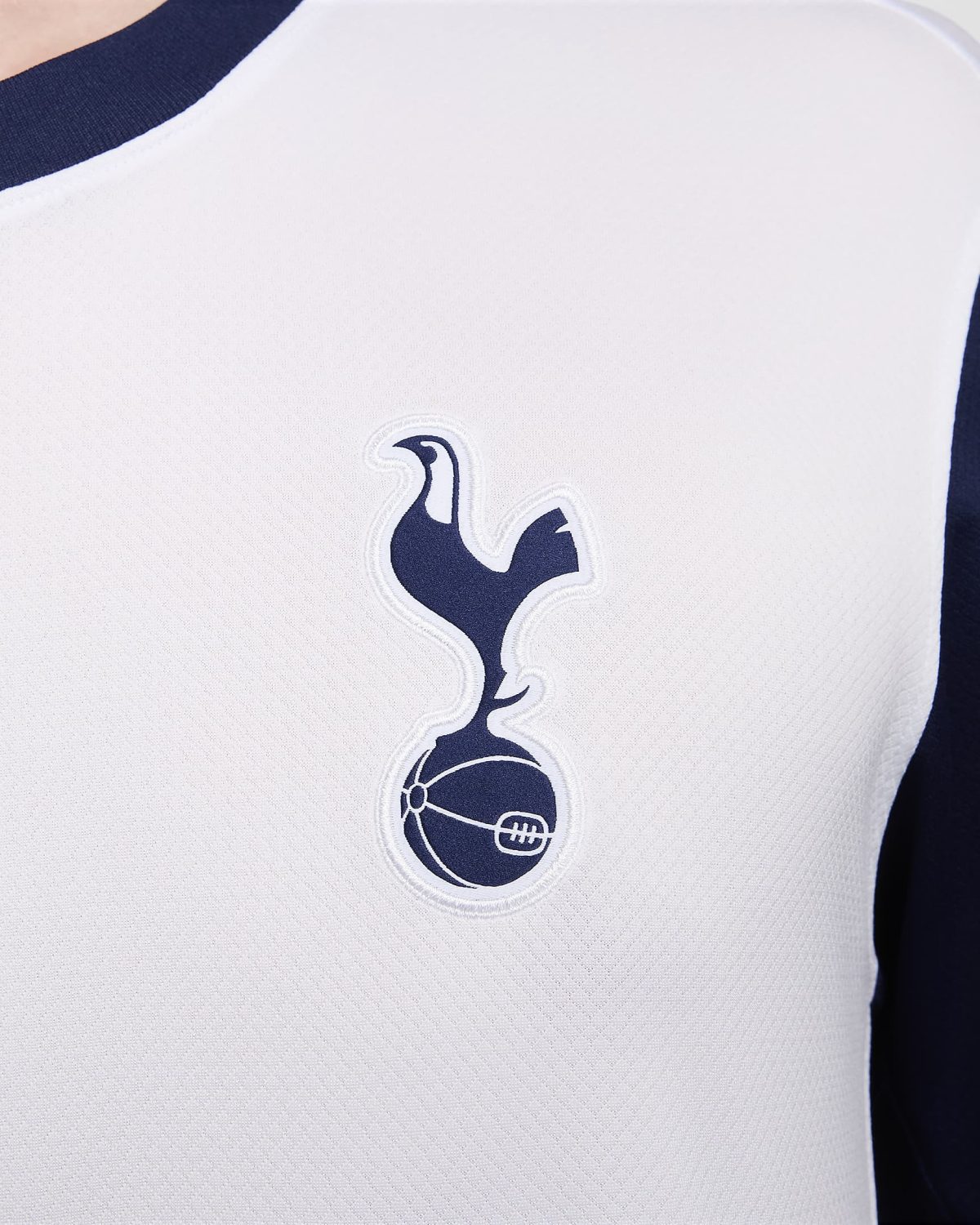 Close-up of a white sports jersey with a navy blue cockerel emblem on the chest and dark navy trim along the neckline pieces.