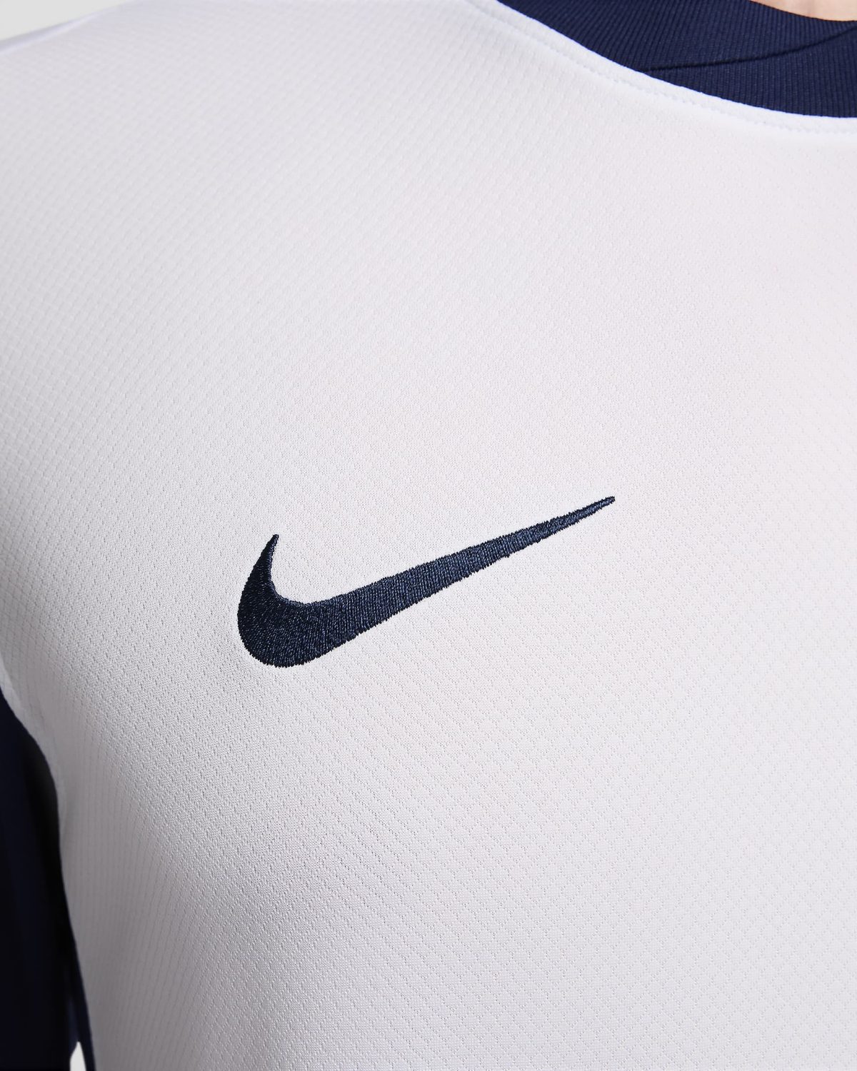 Close-up of white fabric with a navy Nike swoosh logo visible.