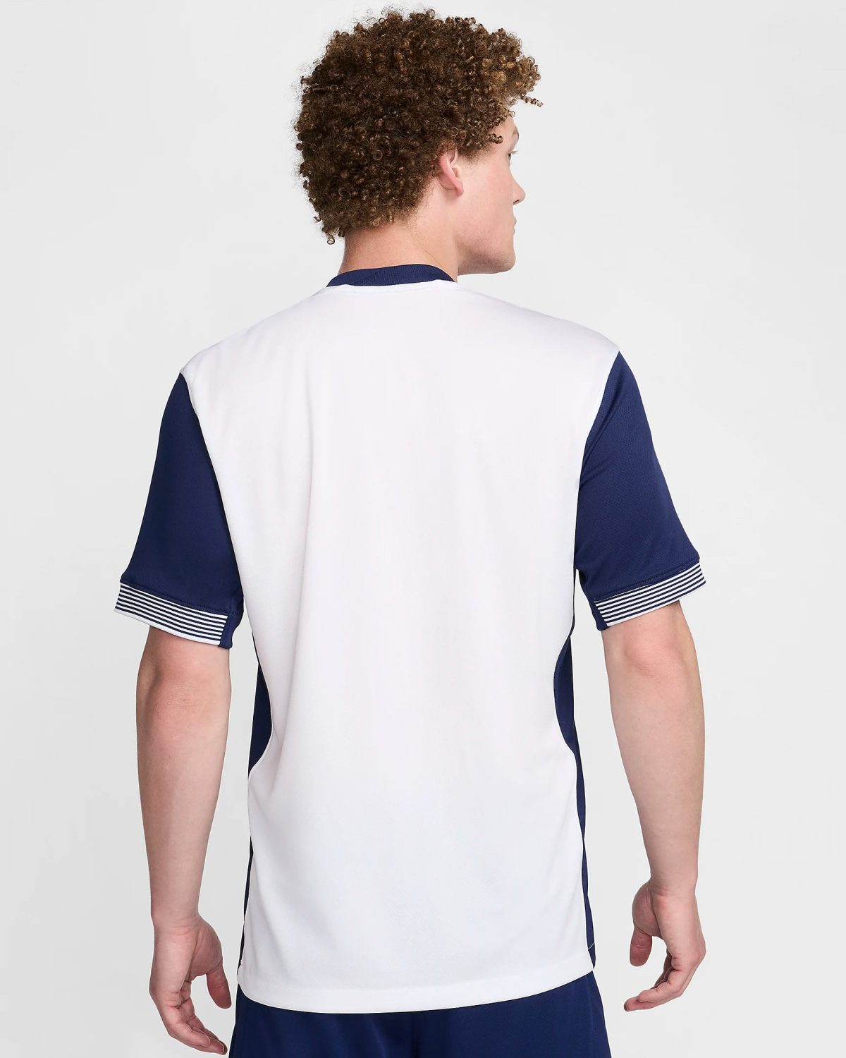 Back view of a person wearing a white and navy sports jersey, standing against a light background.