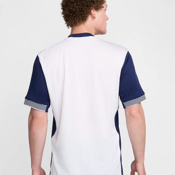 Back view of a person wearing a white and navy sports jersey, standing against a light background.