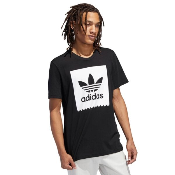 Young man wearing a black T-shirt with a large white Adidas logo on the chest, angled slightly to the side.