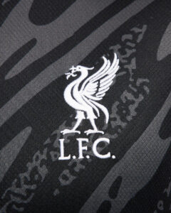 ttlJuVWx5mwfNHB_fe05e79b-b68e-4d3a-a3fd-4e01e14a92a4 | UAE SPORT STORE White embroidered Liver Bird crest with the letters L.F.C. on dark camouflage fabric, representing Liverpool FC against a textured background